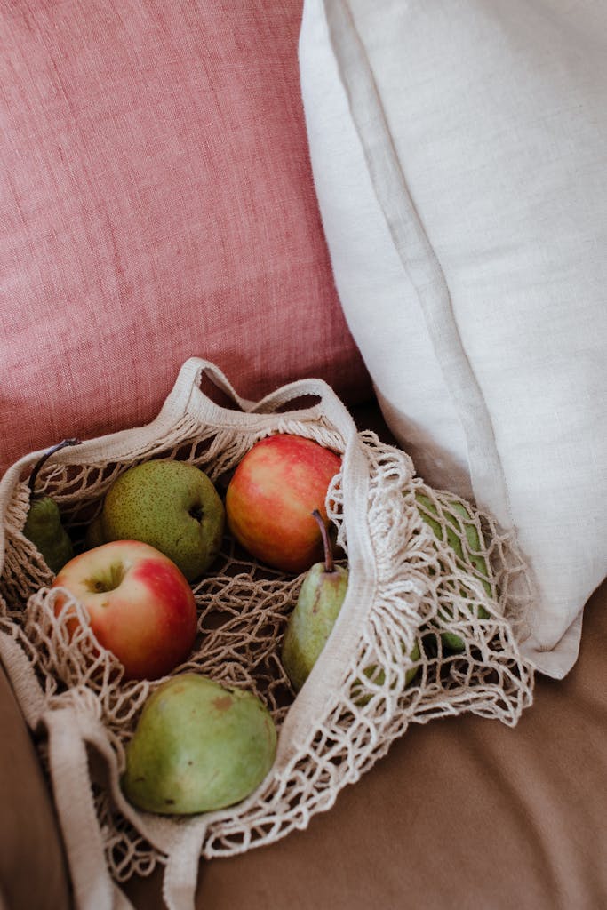 High angle net shopper bag with tasty green and red apples placed on pink comfy couch